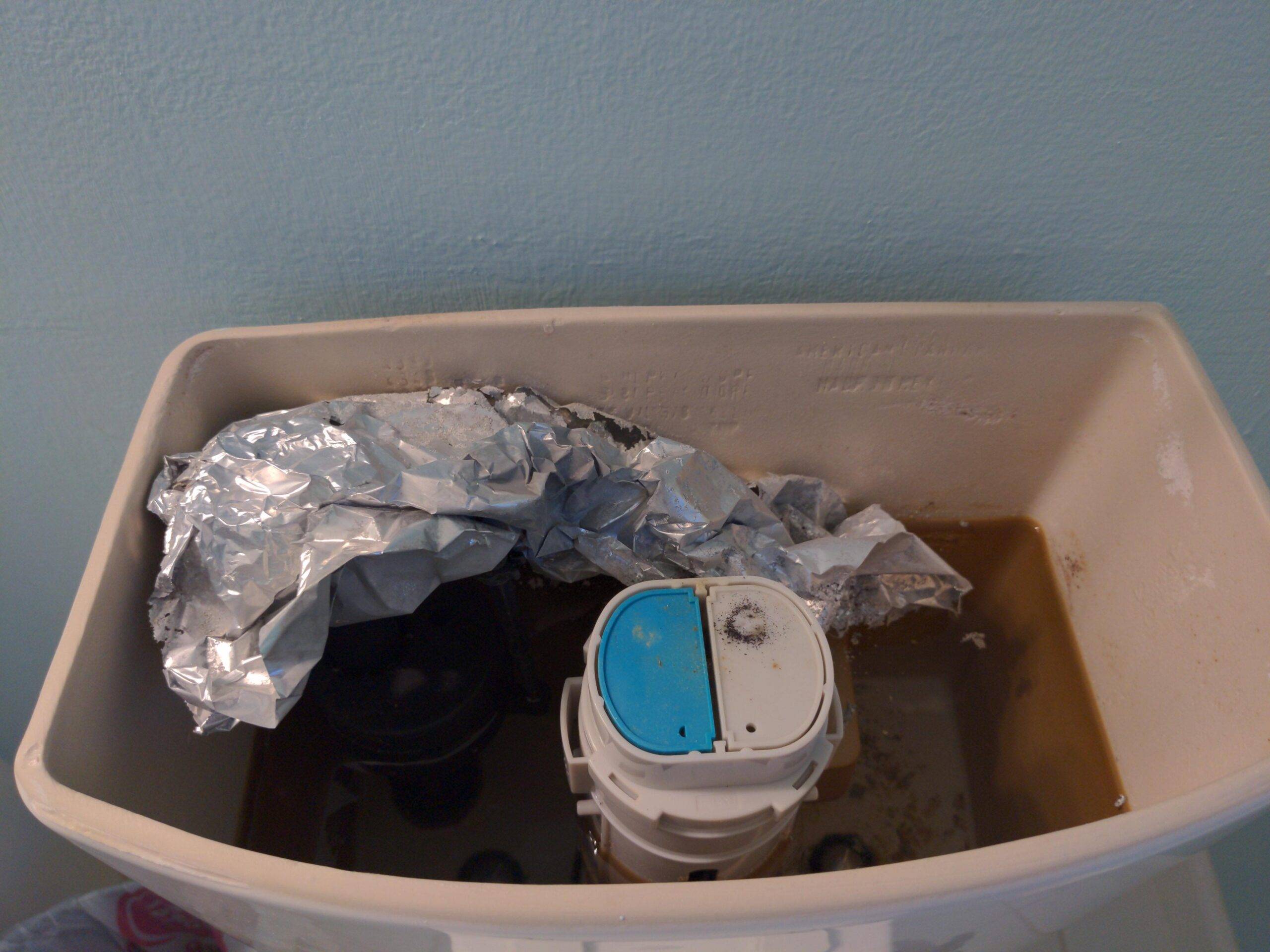 An open toilet tank containing a large amount of aluminum foil.