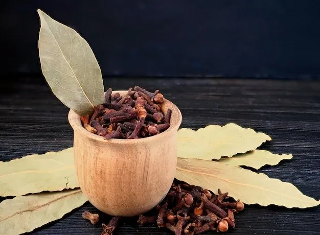 Bay leaves and cloves in a wooden bowl on a black background