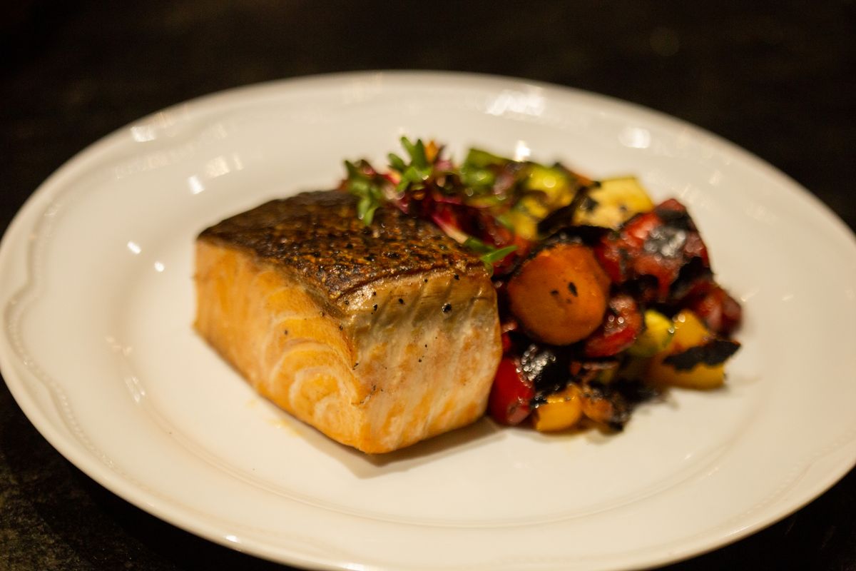 A plate of cooked salmon served with leafy greens and vegetables