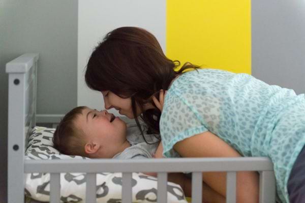 a young brunette woman leans over a child with Down syndrome in bed to give a kiss