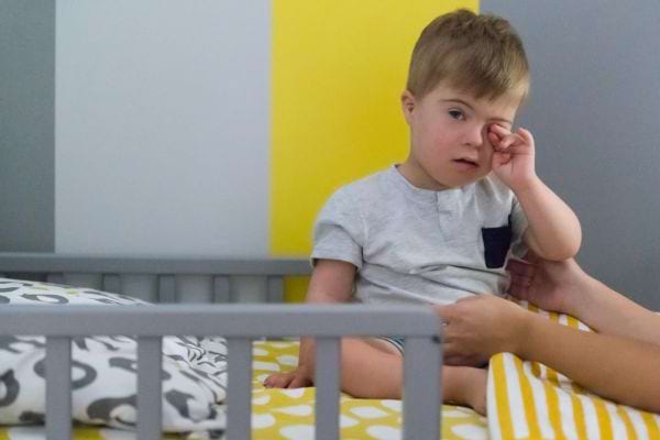 arms reaching out to a child with Down syndrome sitting in bed